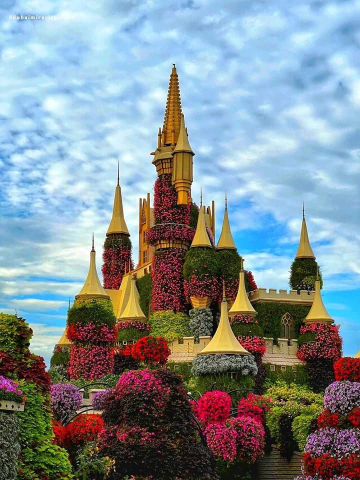 a castle covered in flowers and trees with lots of pink, red and purple flowers