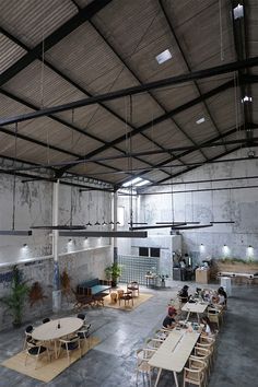 an empty warehouse with tables and chairs in it's center area, while people sit at their desks on the other side