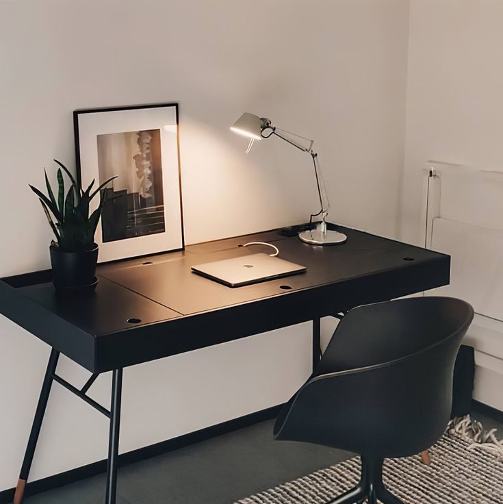 a black desk with a lamp, chair and pictures on the wall in front of it