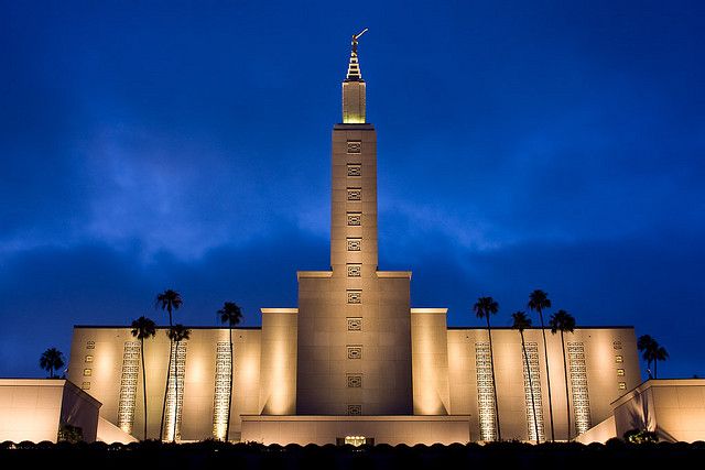 the building is lit up at night with palm trees in front and blue sky behind it