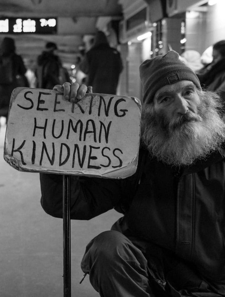 a homeless man holding a sign that says seeking human kindness in front of him