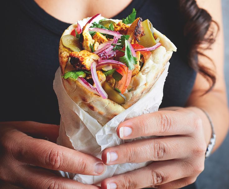 a person holding a pita filled with different types of veggies and meat