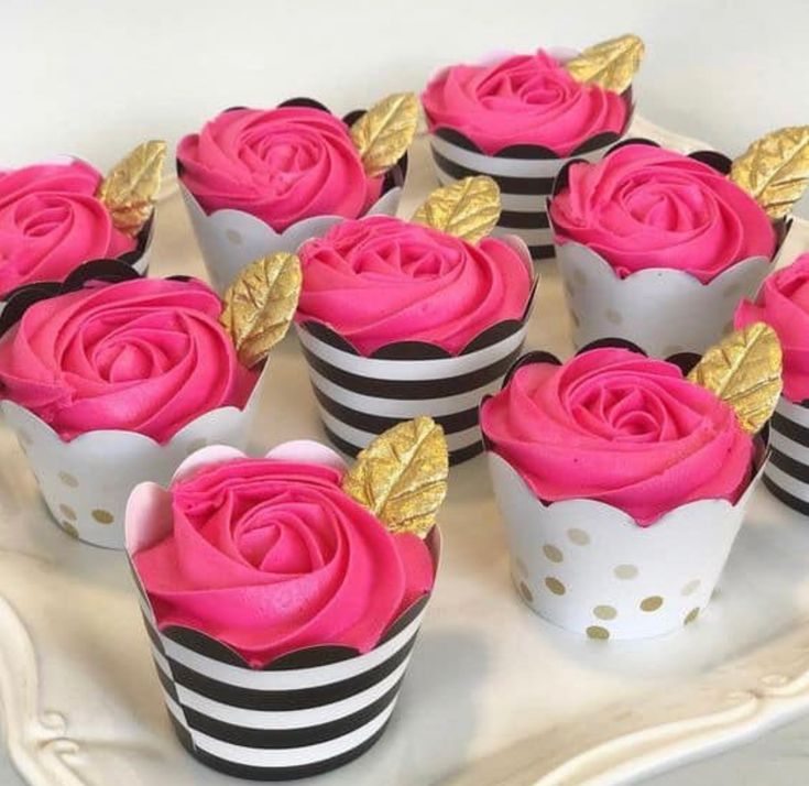 cupcakes decorated with pink frosting and gold leaf decorations on a white plate