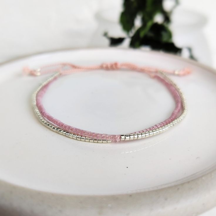 This delicately-strung exclusively crafted bracelet has two strands of tiny Japanese Miyuki glass beads in pink Shell Silk and shiny silver set on natural light pink silk cord. All beads have  a uniform shape with a sparkly finish, perfect for a minimalist look that can be dressed up or down. Finished with a macramé sliding clasp to adjust to your size. **New** Now available with Silver or Gold beads. Please select from variations Also available in Gold/Shell or Turquoise/Copper - https://www.et Dainty Adjustable Silver Beads Bracelets, Adjustable Tiny Beads Wrap Bracelet Gift, Delicate Adjustable Beaded Bracelets, Adjustable Delicate Beaded Bracelets, Delicate Adjustable Bracelet, Dainty Double Strand Beaded Bracelets For Gift, Delicate Beaded Friendship Bracelets As Gift, Delicate Adjustable Silver Beaded Bracelets, Adjustable Pink Beaded Bracelet With Silver Beads