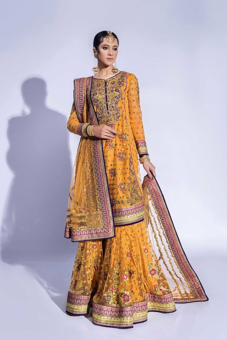 a woman wearing an orange and yellow outfit with matching dupatta, standing in front of