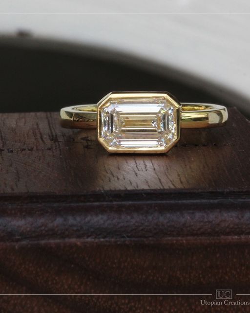 an emerald cut diamond ring sitting on top of a wooden table