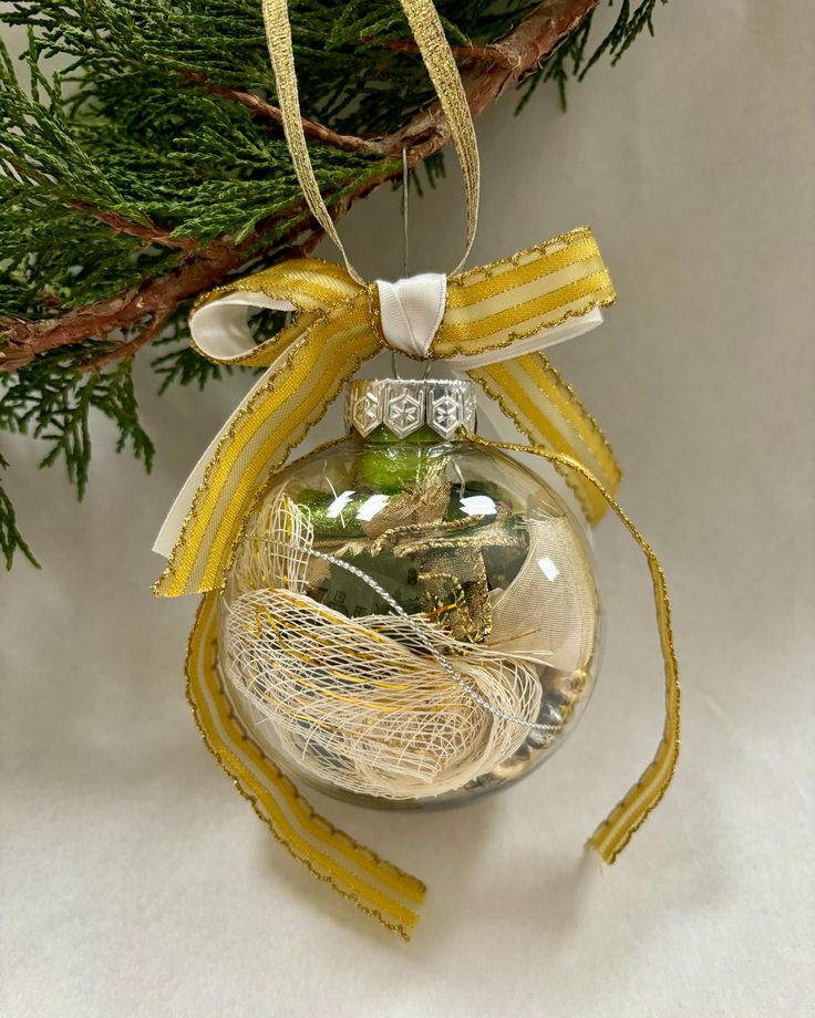 a christmas ornament hanging on a tree branch with yellow ribbon and green balls