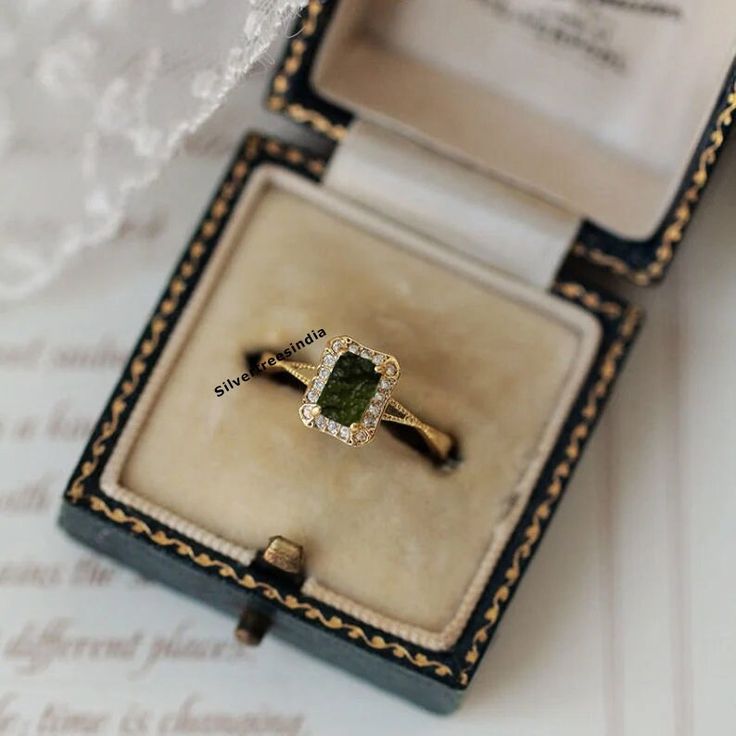 an engagement ring with a green stone sits in a box on top of a piece of paper