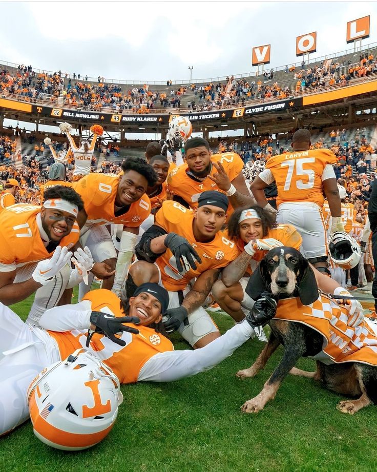 a group of football players posing for a photo with their dog on the sidelines