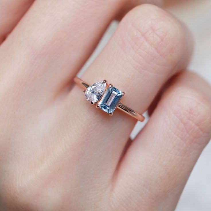 a woman's hand holding an engagement ring with a blue and white diamond in it