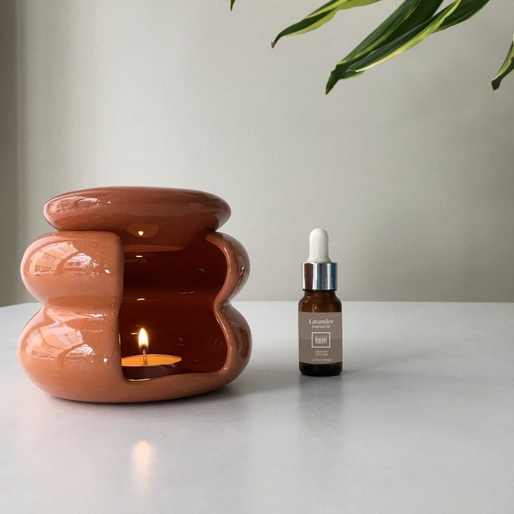 a small candle holder next to an essential oil bottle on a white table with a plant in the background