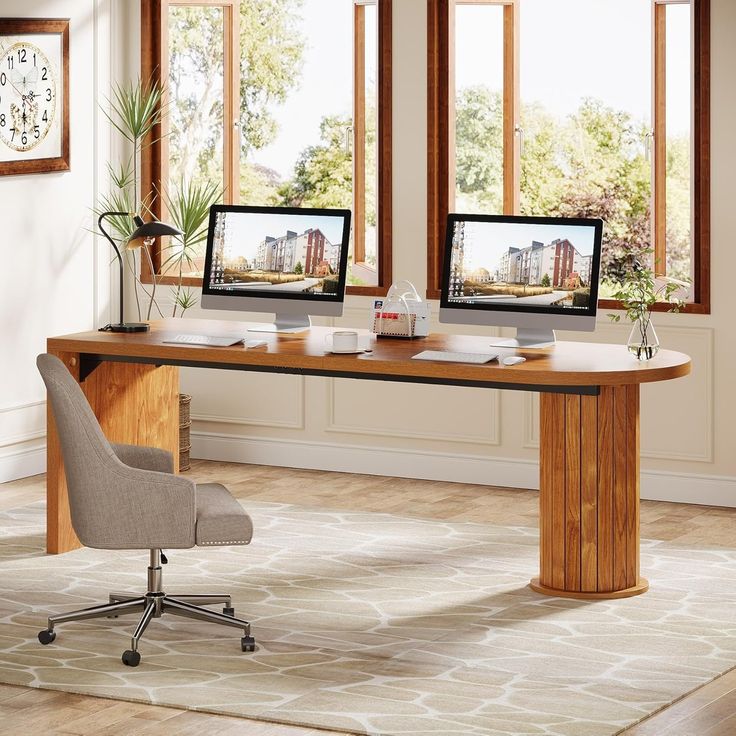 two computer monitors sitting on top of a wooden desk next to a chair and window