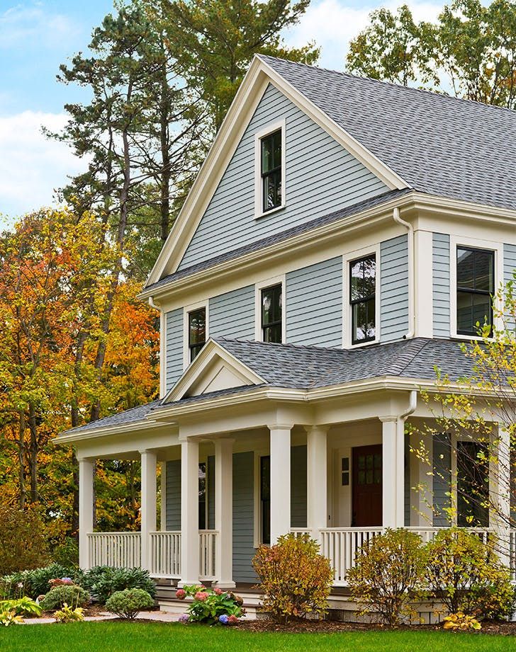 a blue house with white trim on the front porch and two story windows, surrounded by trees