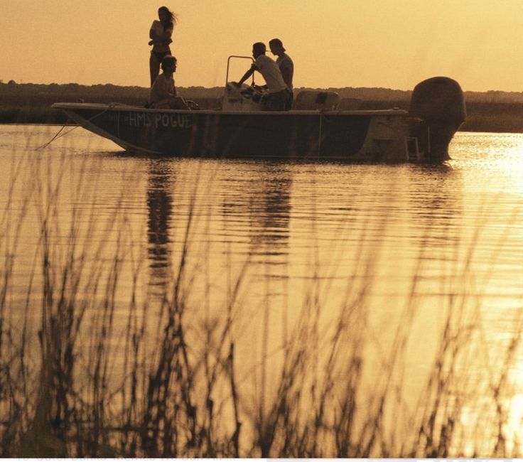 three people on a boat in the water at sunset