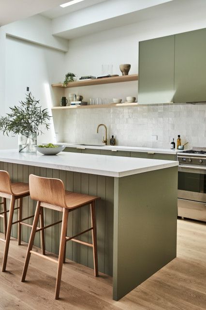 two wooden stools sit in front of an island counter with white countertop and green cabinets