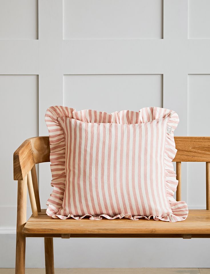 a pink and white striped pillow sitting on top of a wooden bench next to a wall