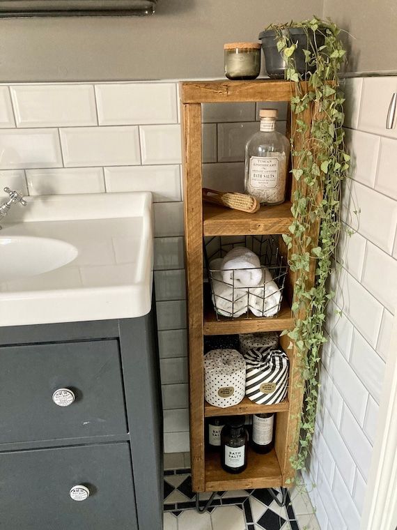 a bathroom with a sink, toilet and wooden shelf in the corner next to a white tiled wall