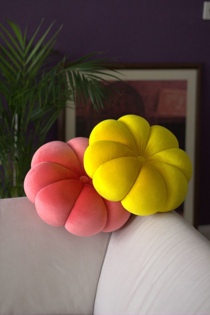 two pillows are sitting on the back of a white couch in front of a potted plant