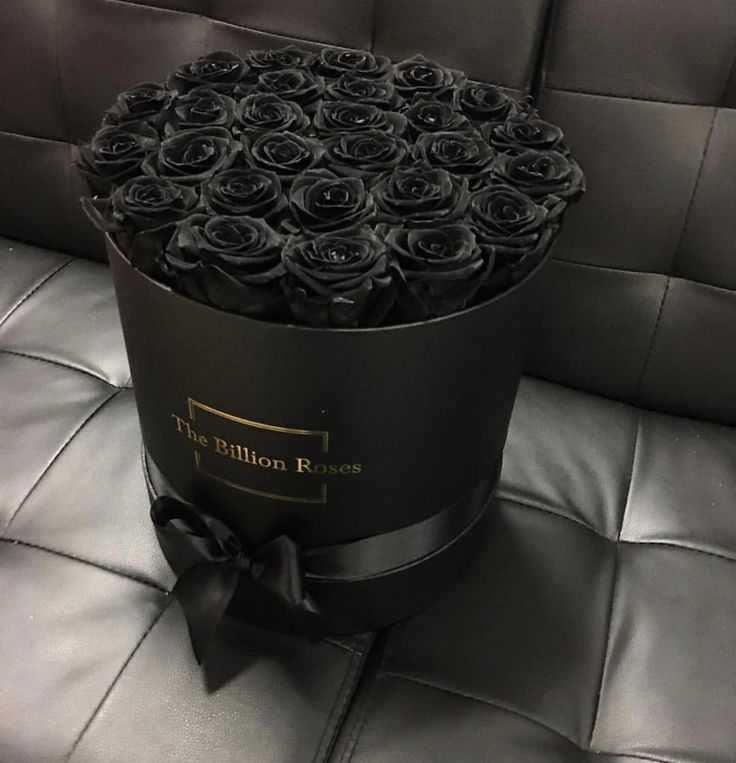 a black box with roses in it sitting on a leather couch next to a pillow