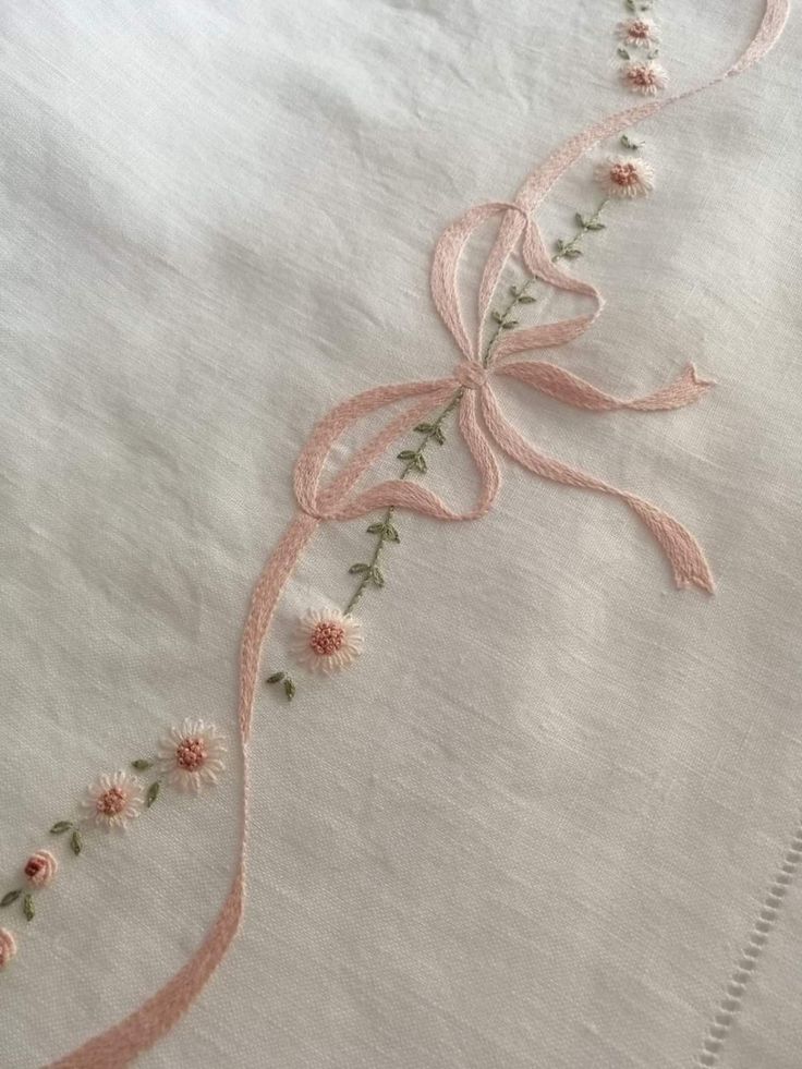 an embroidered piece of cloth with pink flowers and ribbons on it's edge,