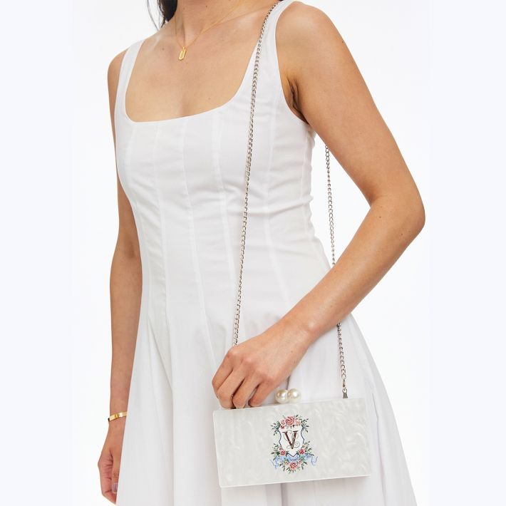 This one-of-a-kind floral crest clutch is perfect for a garden party, bridal shower or wedding. Featuring a stunning white marble design and a mirror inside. A removable chain turns this clutch into a crossbody to complement any gown or sundress. The ornate floral crest can be customized with your initials or family name for a clutch that is truly unique.    8"w x 2"d x 4"h  Acrylic.  Strap: 43"l  Wipe with a damp cloth.  Imported.  Monogramming is vinyl decal. Pearl Handle Clutch For Wedding Guests, White Evening Bag For Spring Party, White Evening Bag With Chain Strap, White Evening Bag With Chain Strap As Gift, Elegant White Clutch For Spring, Elegant Evening Bag For Spring Events, Elegant White Spring Clutch, Elegant Spring Gift Clutch, Summer Wedding Clutch Evening Bag