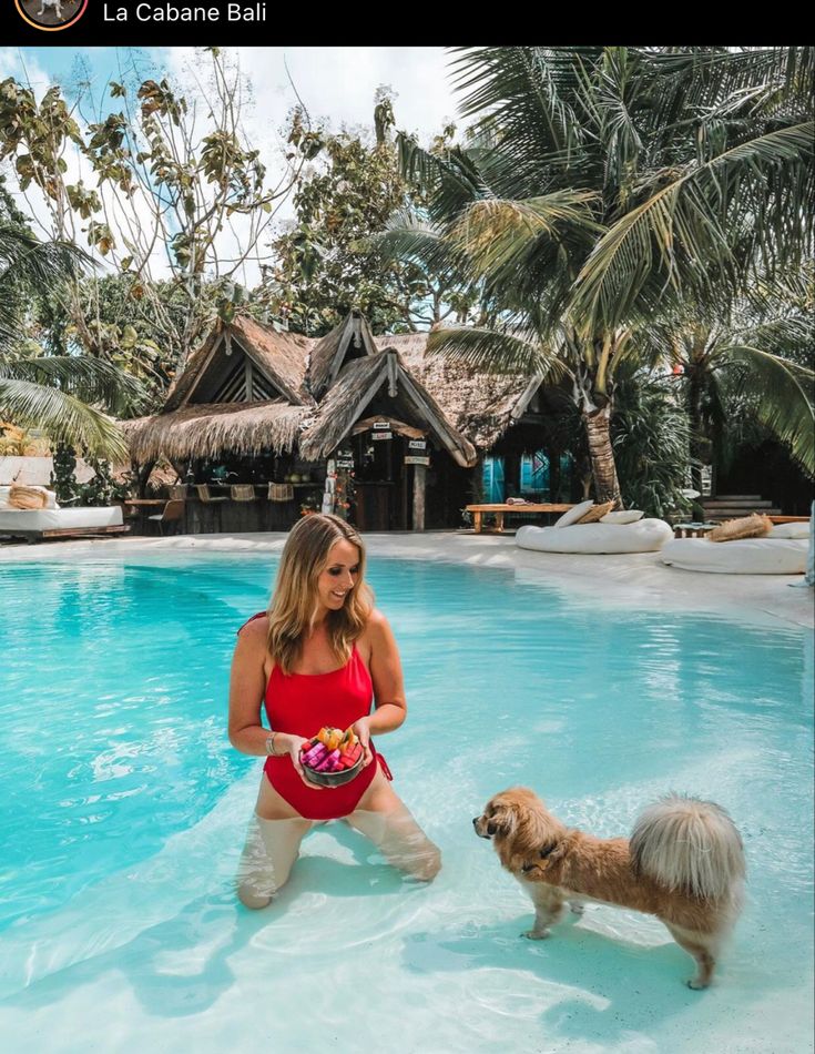 a woman in a red bathing suit standing next to a brown dog near a pool