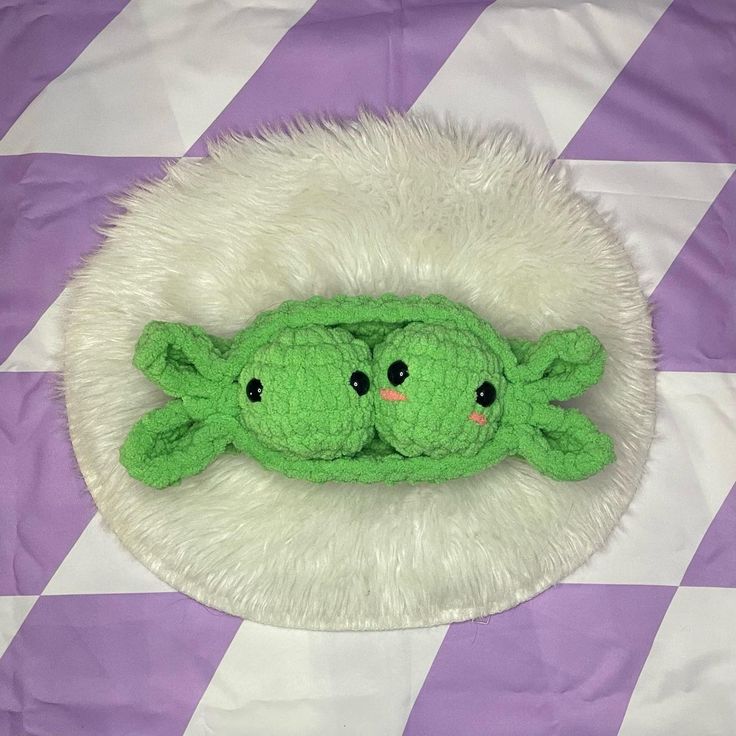 two green stuffed animals laying on top of a purple and white checkered tablecloth