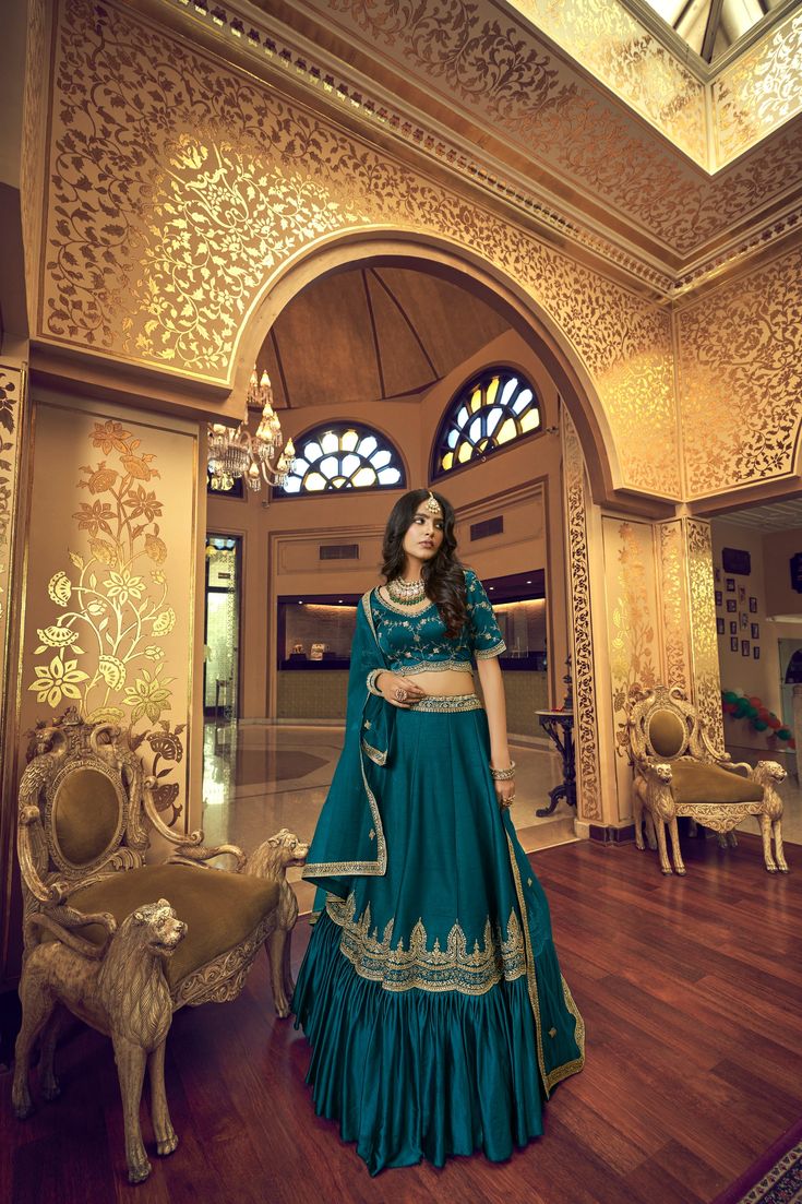 Look stylish in this teal blue 3-piece set, crafted with kumkum silk, lino silk & nylon satin, and heavy net fabric for the blouse, lehenga, and dupatta respectively. Features intricate hand work, zari & sequins embroidery, round neck, regular sleeves, and 10-meter ruffle style flair on the lehenga. The set comes with a dupatta and customizations are available - simply add your measurements during checkout. Dry clean only. No of Set - 3-piece set Color- Teal Blue Blouse Fabric - Kumkum Silk Blou Bollywood Turquoise Saree Set, Designer Turquoise Saree Sets, Blue Art Silk Sets For Traditional Ceremonies, Turquoise Bollywood Designer Wear Sets, Turquoise Bollywood Designer Sets, Elegant Turquoise Festive Set, Bollywood Style Turquoise Set With Dupatta, Bollywood Style Turquoise Sets With Traditional Drape, Bollywood Style Turquoise Festive Sets