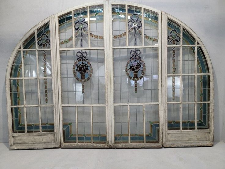 an arched window with stained glass panels and decorative decorations on the windowsill, in front of a white wall