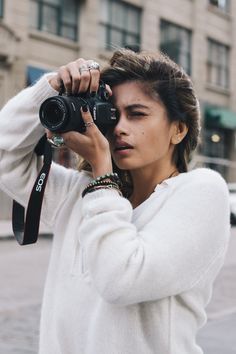 a woman holding up a camera in front of her face while standing on the street