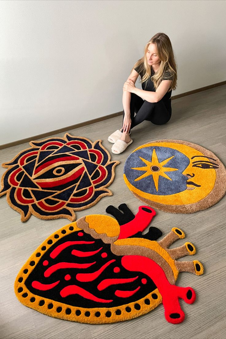 a woman sitting on the floor in front of three circular rugs with different designs