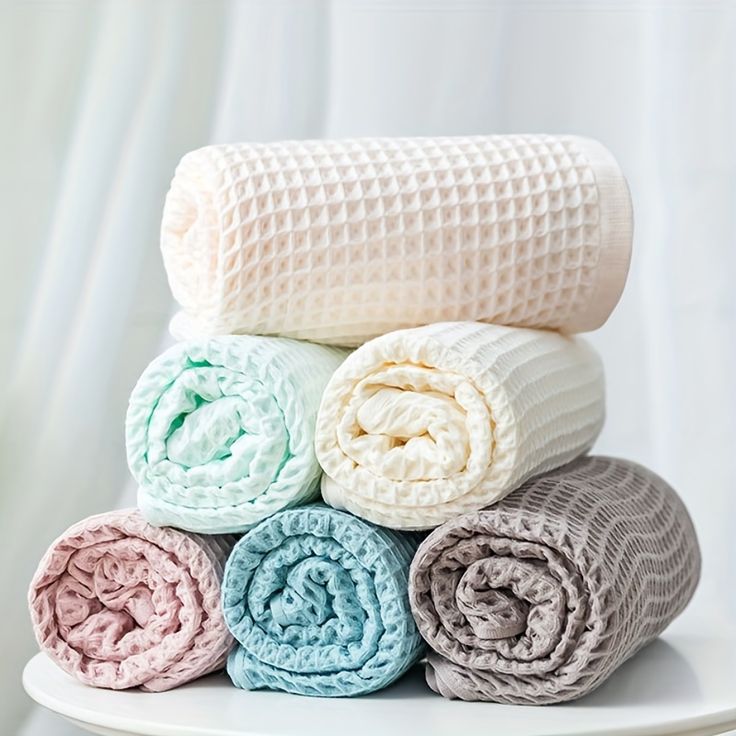 several blankets stacked on top of each other in different colors and sizes, sitting on a white plate