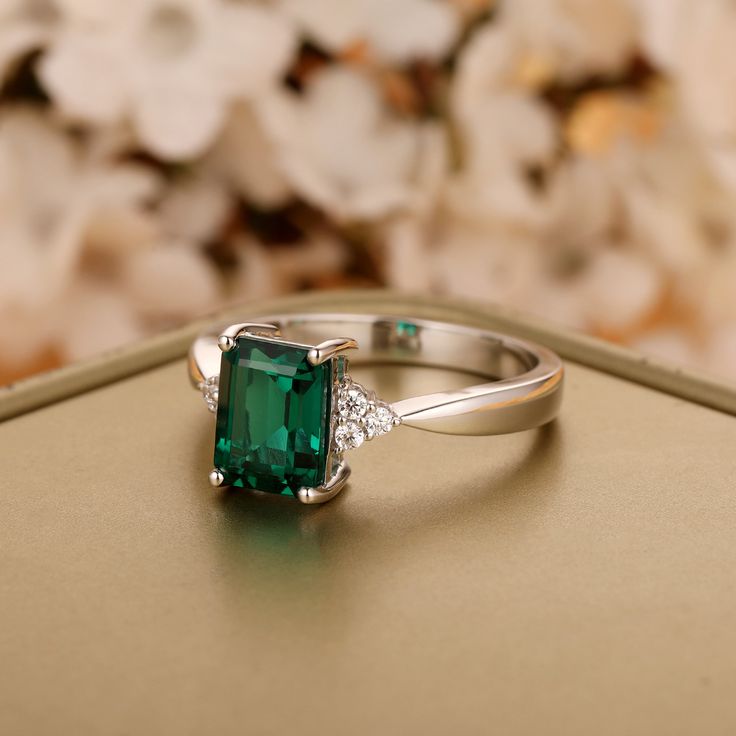 an emerald and diamond ring sitting on top of a gold box with flowers in the background