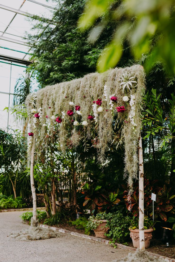 an outdoor wedding ceremony with flowers and greenery hanging from the ceiling in a greenhouse