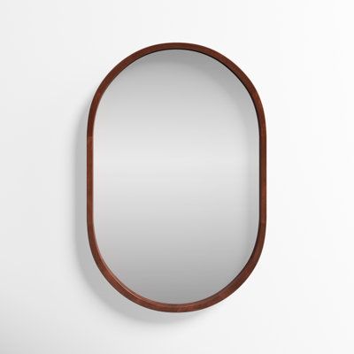 an oval mirror hanging on the wall next to a white wall with a wooden frame