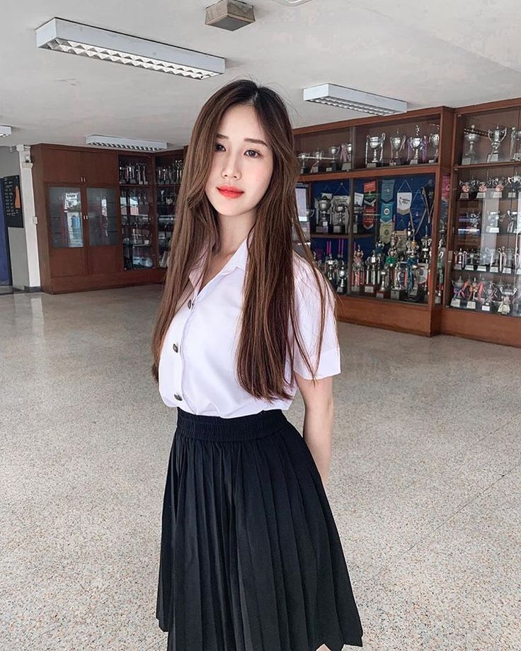 a woman in a white shirt and black pleated skirt posing for the camera with her hands on her hips