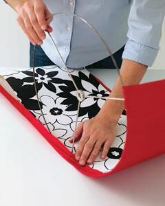 a woman cutting fabric with scissors on top of a piece of red material that has black and white designs