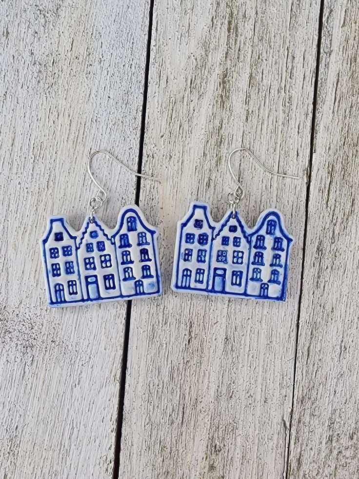 two blue and white ceramic houses are hanging from the side of a wooden plank wall