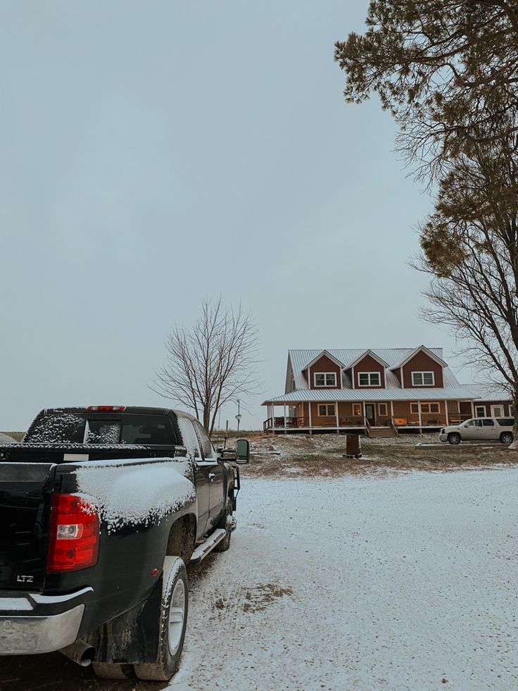 a black truck parked in front of a house on a snow covered field with trees