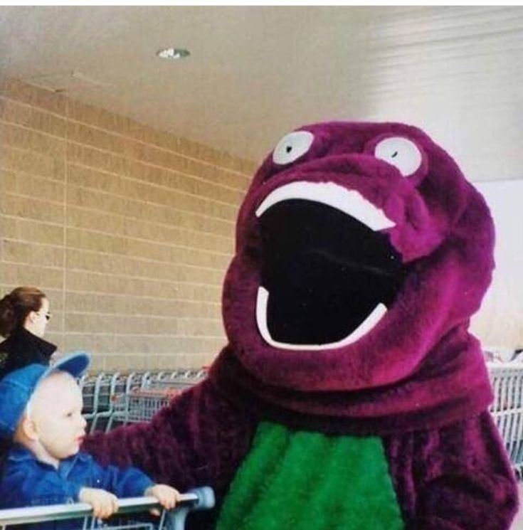 a child in a shopping cart next to a purple monster mascot