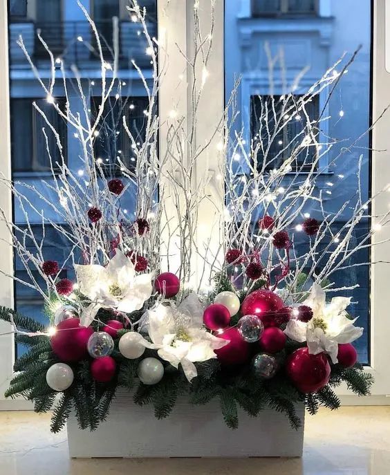 a christmas centerpiece with red and white ornaments in front of a window sill