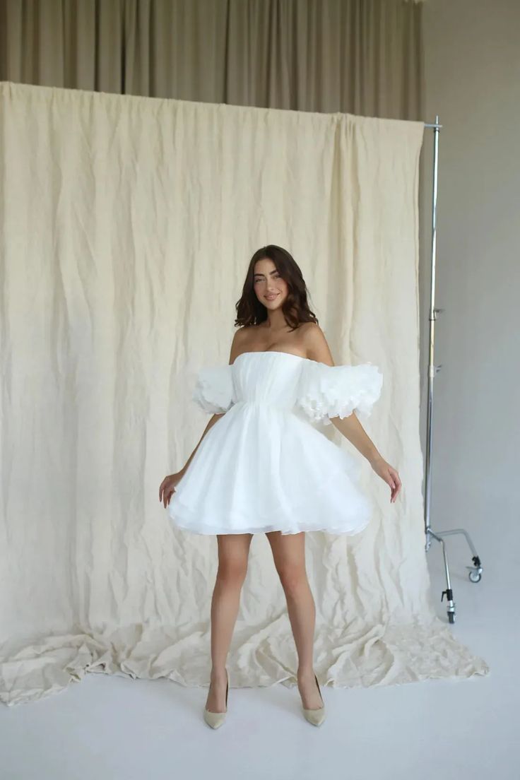 a woman posing in front of a white backdrop wearing a dress with ruffled sleeves