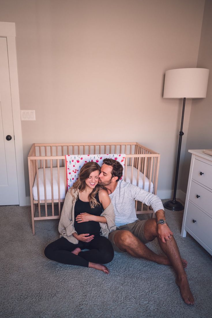 a man and woman sitting on the floor in front of a crib