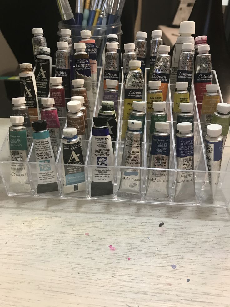 many different types of paint are in plastic containers on a table with pens and pencils