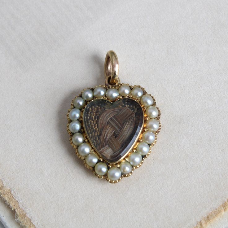 "Circa 1840 an antique Victorian heart-shaped locket charm crafted in 14k yellow gold featuring a beveled-glass covered compartment holding a beautifully woven love-knot of chestnut brown hair. With the pearl surround (likely natural pearls but not tested) set in cut-down collets and the back extravagantly chased in a lush acanthus leaf pattern and \"B. Hunter\" engraved on a ribbon banner, it's a poignant and rare example of early Victorian mourning jewelry. Measuring approximately 7/8\" north Vintage Charm Jewelry For Valentine's Day Formal, Vintage Charm Jewelry For Valentine's Day Formal Occasion, Formal Vintage Charm Jewelry For Valentine's Day, Victorian Medallion Jewelry With Heart Charm, Victorian Heart Charm Jewelry For Formal Occasions, Victorian Locket Jewelry For Valentine's Day, Victorian Locket For Valentine's Day, Antique Yellow Gold Jewelry With Heart Charm, Victorian Yellow Gold Jewelry For Valentine's Day