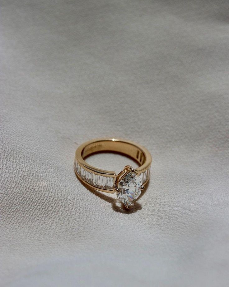 a gold ring with a single diamond on it sitting on a white cloth covered surface