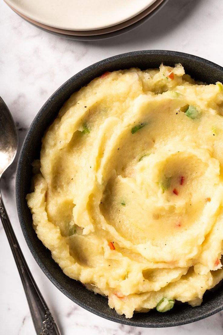 mashed potatoes in a black bowl on a white marble counter top with silverware