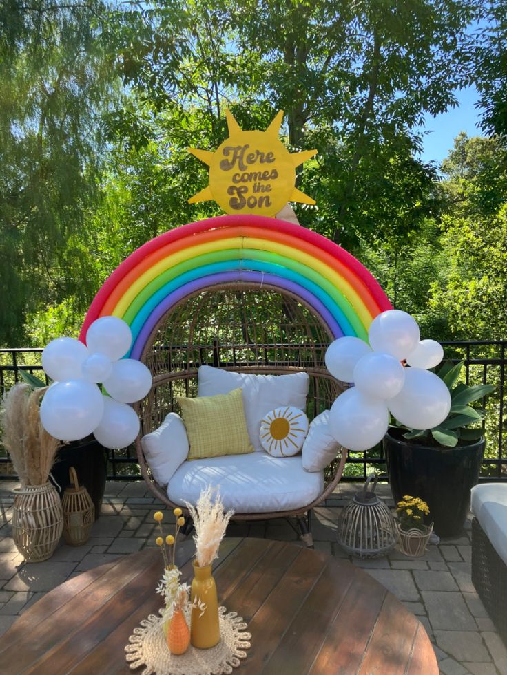 a white chair sitting on top of a wooden floor next to a rainbow arch with balloons