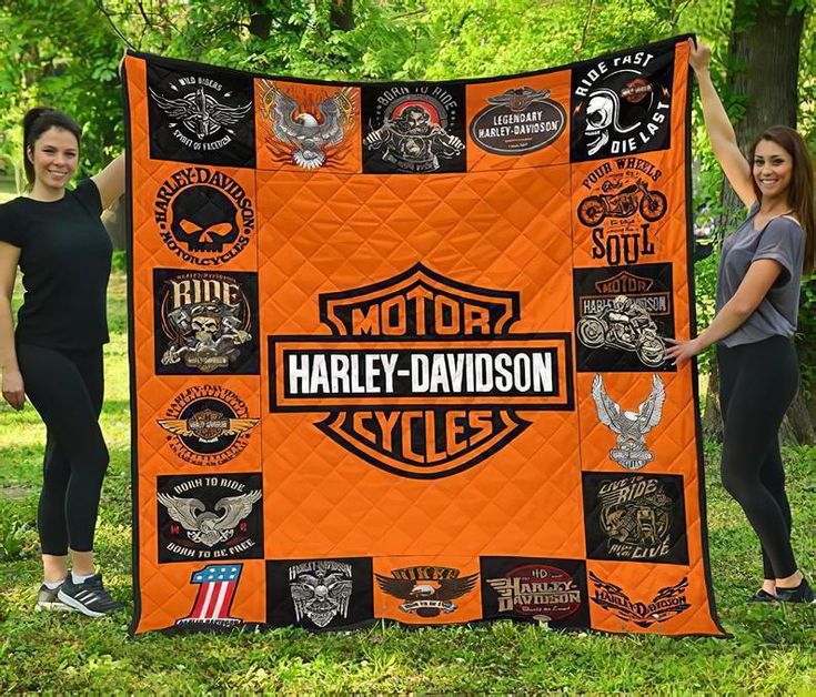 two women standing next to an orange harley davidson quilt