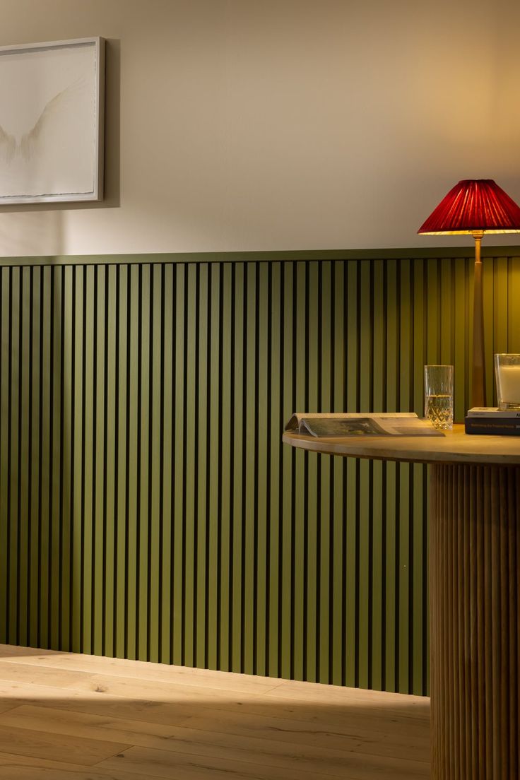 a green striped wall in a room with a lamp on the table and pictures above it